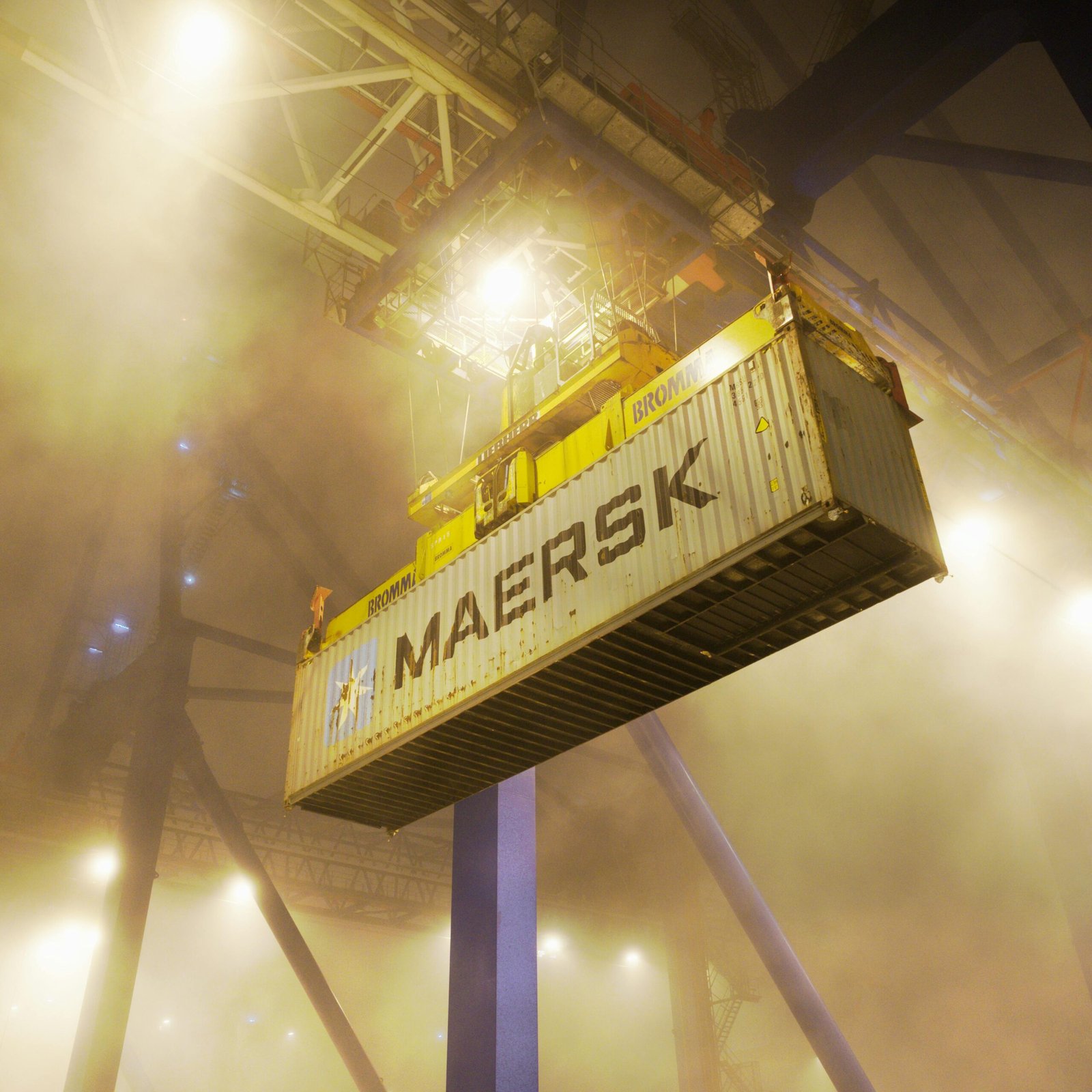 Industrial shipping container suspended by crane in Gdańsk port at night.